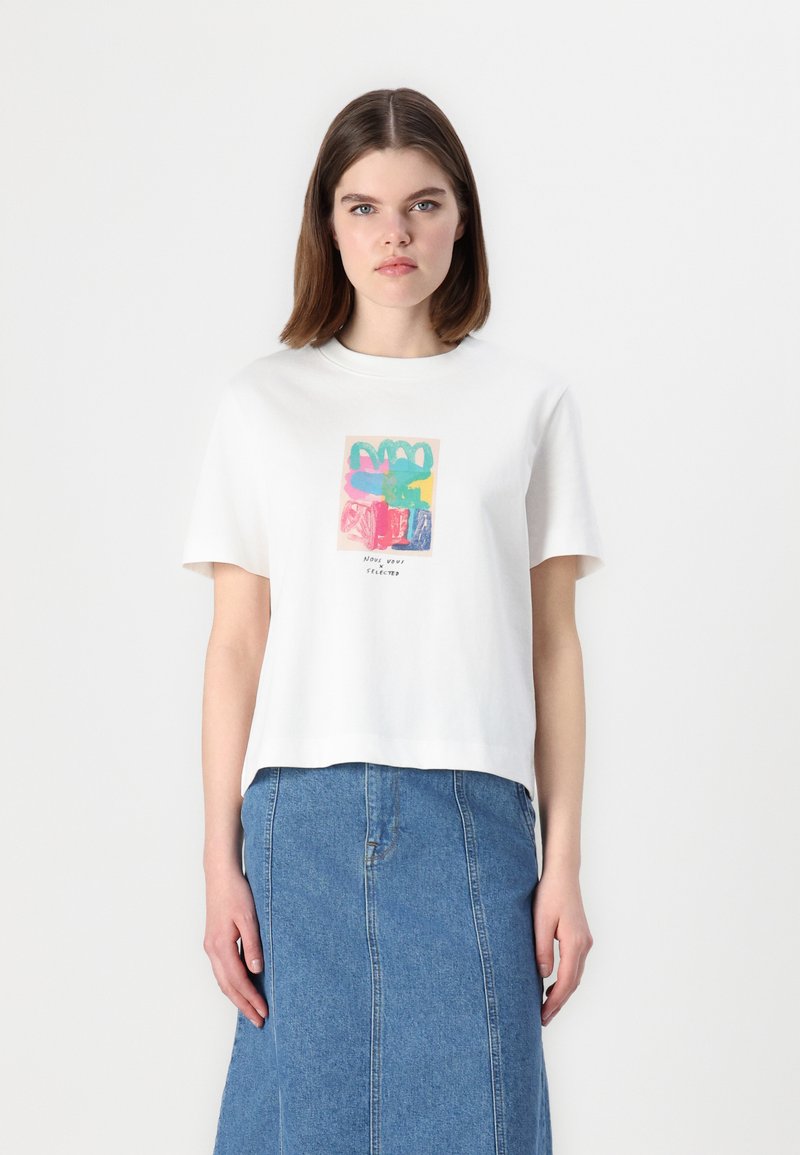 T-shirt en coton blanc à manches courtes avec un imprimé graphique abstrait coloré centré sur le devant. Porté avec une jupe en denim.