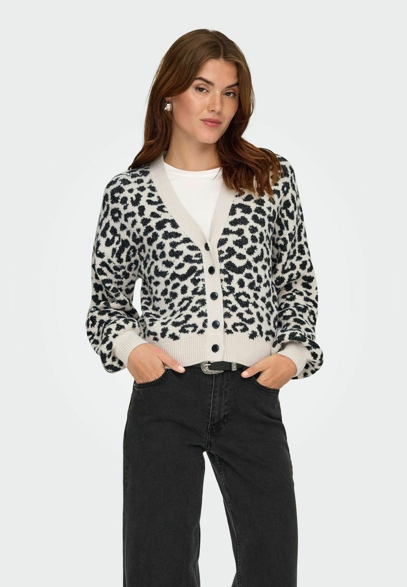 Leopardmönstrad cardigan i beige och svart, med v-ringning, knäppning och ribbade ärmslut. Matchas med högmidjade svarta jeans.