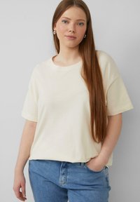 Lichtcrème, T-shirt met korte mouwen van katoen. Heeft een ronde halslijn en een ontspannen pasvorm, gecombineerd met blauwe denim jeans.