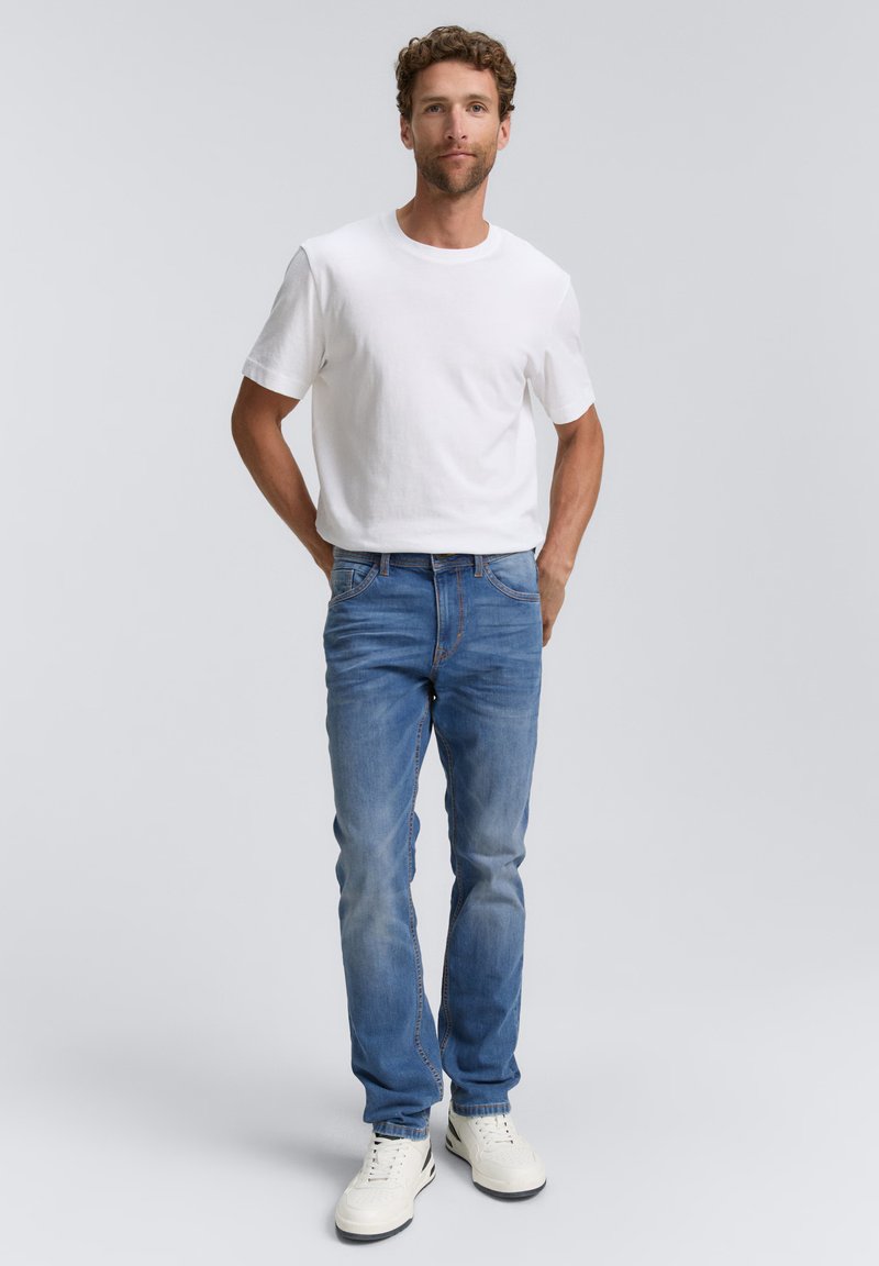Camiseta de algodón blanca combinada con jeans de mezclilla azul medio. Los jeans tienen un corte clásico con un ligero desvanecimiento, complementados con zapatillas blancas.