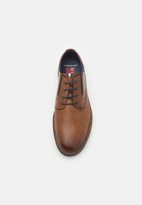 Brown leather lace-up shoe with perforated texture, round toe, and a contrasting rubber sole. Interior features a blue insole labeled "Comfort Wide."