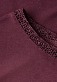 Burgundské tričko s texturovanou krajkovou páskou kolem výstřihu, vyrobené z měkké bavlny s hladkým povrchem.