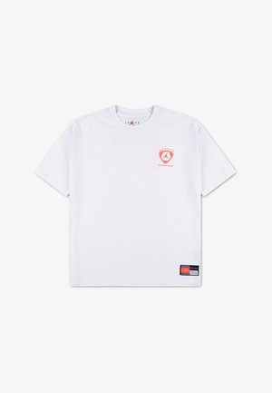 Hvid T-shirt med korte ærmer, lille rødt Jordan-logo på venstre bryst og et sort og rødt mærke nær nederste søm. Ingen synlige personer.