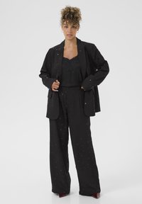 Schwarzes Blazer- und weit geschnittenes Hosen-Set mit aufwändigen bestickten Mustern. Der Oberteil hat Spitzendetails. Der Stoff ist strukturiert und leicht.