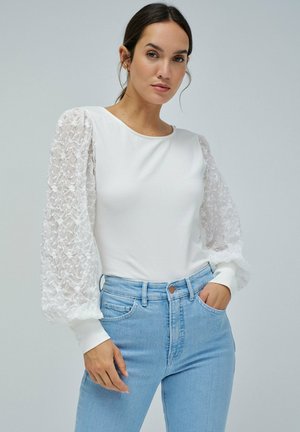 Top blanco de manga larga con mangas abullonadas, texturizadas y transparentes; diseño de cuello redondo; combinado con jeans de cintura alta en azul claro.