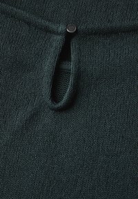 Tissu tricoté texturé vert foncé avec une ouverture en forme de clé et une fermeture à pression en métal en haut pour un maintien sécurisé.