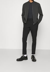 Szara kurtka bomber o prążkowanej fakturze, czarne dopasowane spodnie, czarne sznurowane buty oraz białe skarpetki. Prosty fason z zamkiem błyskawicznym.