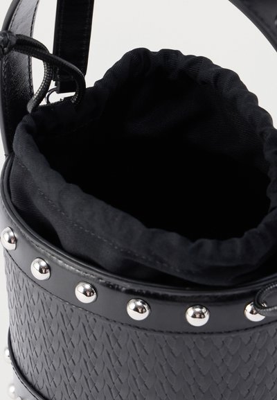 Μαύρη τσάντα τύπου κάδος με υφή πλεκτού, με σφικτό υφασμάτινο πάνω μέρος, μεταλλικά τρουκς στο σώμα και ομαλές μαύρες λαβές. Το εσωτερικό είναι επενδυμένο με ύφασμα.