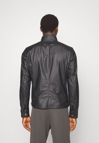 Svart läderjacka med hög krage, långa ärmar och dekorativ sömnad. Inkluderar knäppning vid ärmsluten och en skräddarsydd passform.