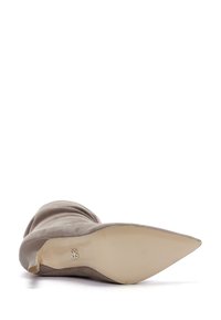 Bota de tacón alto con punta afilada y parte superior de ante gris claro, tacón cónico y suela beige lisa con un detalle del logo de la marca.