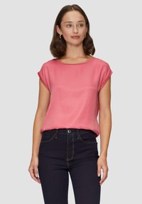 Korte mouwen, relaxte top van zachte, blush roze stof. Heeft een bootnek en een gladde textuur, gecombineerd met donkerdenim jeans.