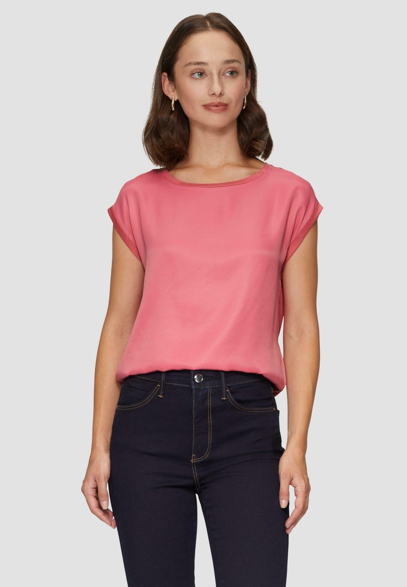 Korte mouwen, relaxte top van zachte, blush roze stof. Heeft een bootnek en een gladde textuur, gecombineerd met donkerdenim jeans.