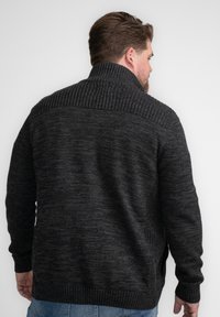 Suéter de punto gris oscuro con cuello alto, con una textura de canalé en los hombros y bolsillos laterales. Presenta un suave patrón moteado.