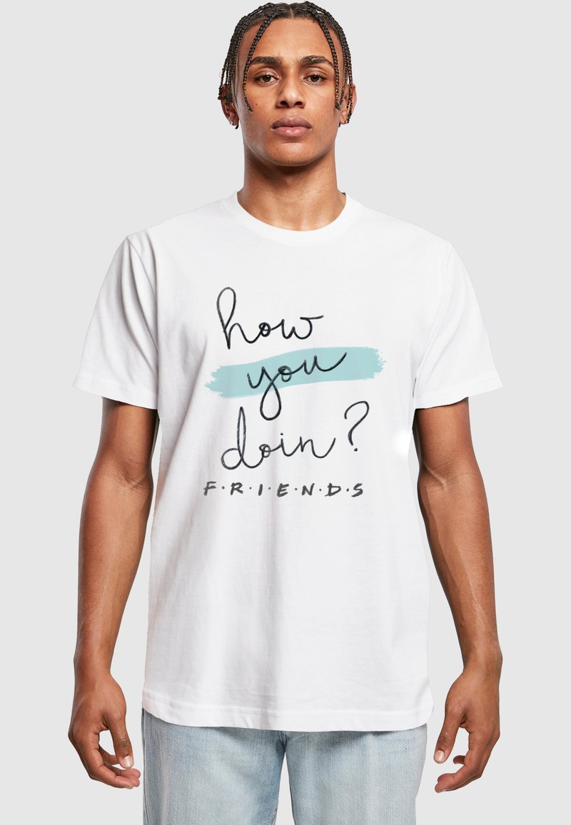 Camiseta de algodón blanca con el texto negro "¿cómo te va?" y "F.R.I.E.N.D.S." sobre un fondo de pinceladas azules. Mangas cortas, corte relajado.