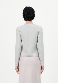 Grå langermet topp med rund hals, kort design og myk tekstur. Lyserosa skjørt synlig under, som viser en enkel, ren estetikk.