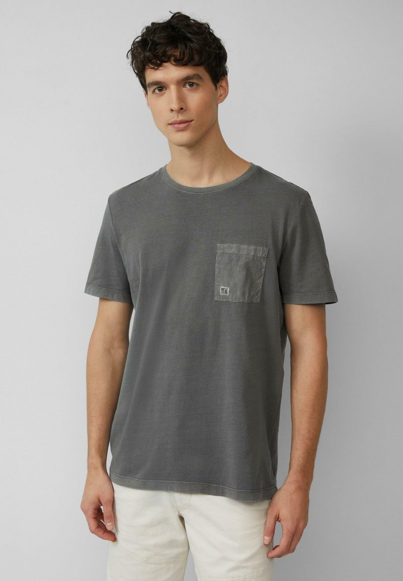 Grijze katoenen T-shirt met een ronde hals, korte mouwen en een patchzak op de linkerkant van de borst. Zachte textuur met minimale stikseldetails.