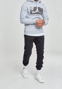 Felpa grigia con stampa grafica, abbinata a pantaloni jogger neri. Scarpe da ginnastica bianche e calzini bianchi visibili completano l'outfit.