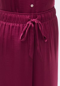 Pantalon en tissu bordeaux avec une taille froncée et un nœud coulissant pour un ajustement personnalisé, agrémenté d'un petit bouton sur le devant.