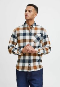 Camicia in flanella a quadri color marrone, beige e blu navy. Presenta un colletto button-down, una tasca sul petto e maniche lunghe con polsini a bottoni.