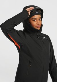Zwarte waterdichte jas met een capuchon, oranje zijaccenten, een ritssluiting aan de voorkant en twee ritszakken. De stof lijkt glad en duurzaam.