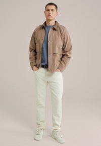 Conjunto informal que incluye una chaqueta ligera marrón con cuello, un suéter azul, pantalones de color claro y zapatillas blancas.