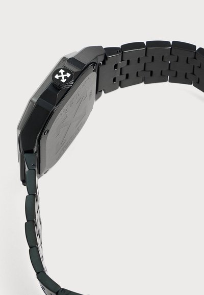 Montre-bracelet en métal noir avec un bracelet à maillons, vue latérale visible centrée sur la couronne de la montre avec un symbole de croix blanche.