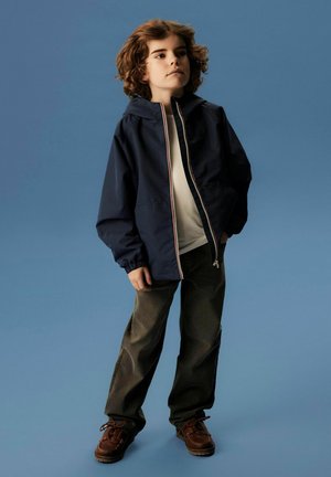 Marine windbreaker met een capuchon, ritssluiting en elastische manchetten. Draag het over een wit shirt en combineer het met donkergroene broeken en bruine schoenen.