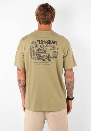 T-shirt en coton vert olive avec un graphisme au dos représentant un personnage de dessin animé modelant une planche de surf, avec le texte "FISH & SHAPE" au-dessus.