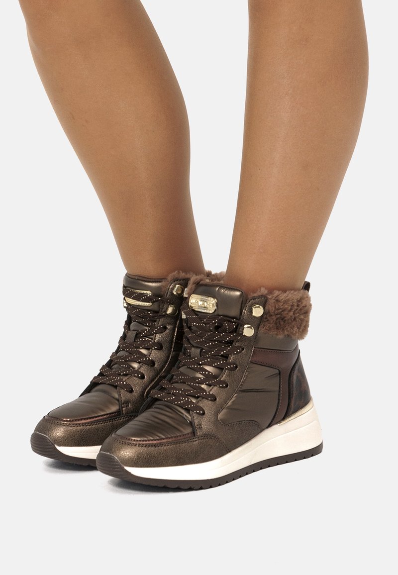 Braune High-Top-Sneakers mit Kunstfellbesatz am Knöchel, strukturierten Lederpaneelen, Metallbeschlägen und einer weißen Gummisohle.