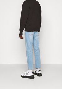 Černá mikina, světle modré džíny a bílé tenisky s černými akcenty. Materiál vypadá jako bavlna, s volným střihem a minimálními detaily.