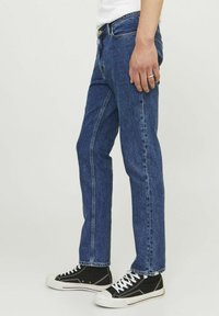 Blugi din denim de culoare bleu închis, cu croială dreaptă, cusături vizibile și o ușoară decolorare. Asortați cu adidași negri cu fața înaltă.
