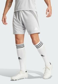 Grå idrottsshorts med sidosträck, elastisk midja och vita detaljer. Parat med vita strumpor och fotbollsskor med svarta detaljer.