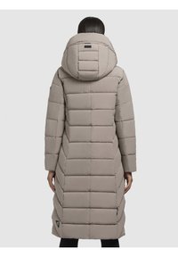 Cappotto lungo imbottito di colore beige chiaro con un grande cappuccio. Presenta un motivo a cuciture rettangolari, cerniere laterali e un piccolo logo sulla zona del collo.