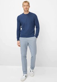 Marineblauer Strickpullover mit rundem Ausschnitt, kombiniert mit hellblauen Slim-Fit-Hosen und weißen Turnschuhen mit blauen Akzenten.