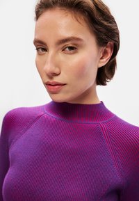 Sweater roxo canelado com gola alta. Apresenta um design texturizado e ajustado, com listras vermelhas subtis que correm verticalmente.