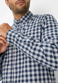 Blauw-wit geruite button-up blouse van stof, met een kraag en lange mouwen met knoopmanchetten.