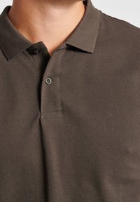 Brązowa koszulka polo z teksturowanej tkaniny, z klasycznym kołnierzykiem, zapinana na dwa guziki i z subtelnymi detalami w przeszyciach.