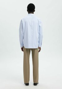 Camisa de manga larga a rayas azul y blanca con cuello clásico, combinada con pantalones beiges. Tejido suave con un corte relajado y dobladillo recto.