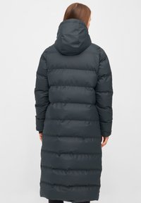 Lange donkergrijze pufferjas met een capuchon, met een doorgestikt ontwerp en elastische manchetten. De stof lijkt glad en geïsoleerd, en reikt tot halverwege het scheenbeen.