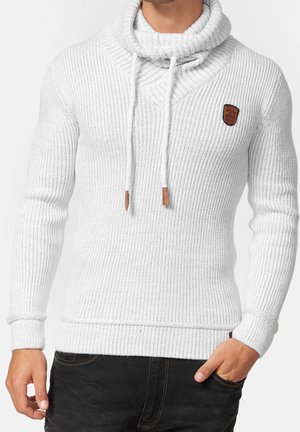 Pull blanc en maille côtelée avec un grand col cheminée, des cordons de serrage et un patch logo en cuir marron. Tissu texturé et coupe ajustée.