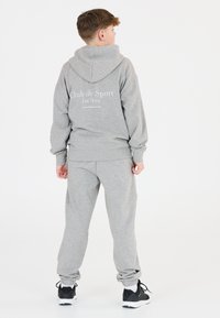 Grau, weicher Stoff-Trainingsanzug mit kapuzenpulli und passenden Hosen. Auf der Rückseite steht der Text "Club de Sport Les Arcs" in Weiß.