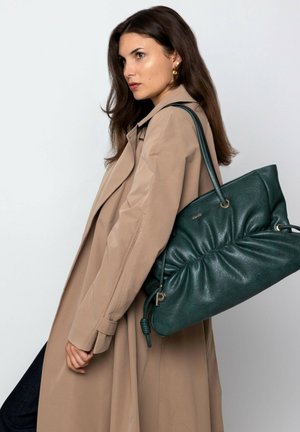 Green leather shoulder bag with gathered texture, secured by a knot detail; displayed alongside a beige trench coat.