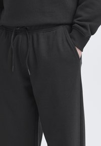 Black cotton sweatpants featuring a drawstring waist, side pockets, and ribbed cuffs, with a soft texture and relaxed fit.