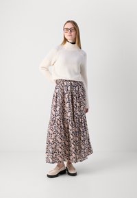 Krém színű bordázott pulóver magas nyakkal, párosítva egy hosszú, virágmintás navy és rózsaszín szoknyával, valamint bézs slip-on cipőkkel, fekete talppal.