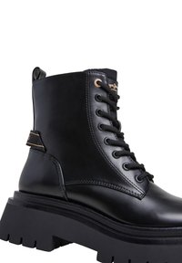 Stivaletto in pelle nera con suola di gomma spessa, dotato di lacci frontali, linguetta laterale e dettagli in metallo color oro.
