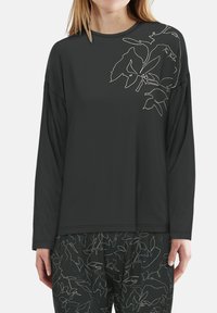 Woman wearing a dark long-sleeve top with light-colored botanical line art on the shoulder, paired with matching patterned pants.