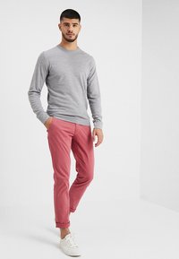 Ljusgrå mjuk tyg crewneck-tröja i kombination med uppvikta ljusrosa byxor och vita sneakers. Slim-fit silhuett, avslappnad design.