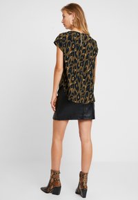 Top a maniche corte con stampa leopardata in tonalità terrose, abbinato a una gonna in pelle nera e stivaletti marroni a motivo. Texture liscia su tutta la superficie.