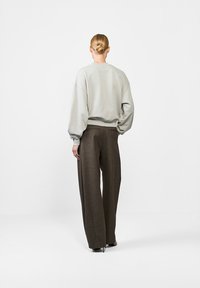 Jasnoszary, oversize sweter z opadającymi ramionami i żebrowanym dołem, w połączeniu z brązowymi szerokimi spodniami z teksturowanej tkaniny.