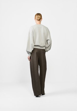 Jasnoszary, oversize sweter z opadającymi ramionami i żebrowanym dołem, w połączeniu z brązowymi szerokimi spodniami z teksturowanej tkaniny.